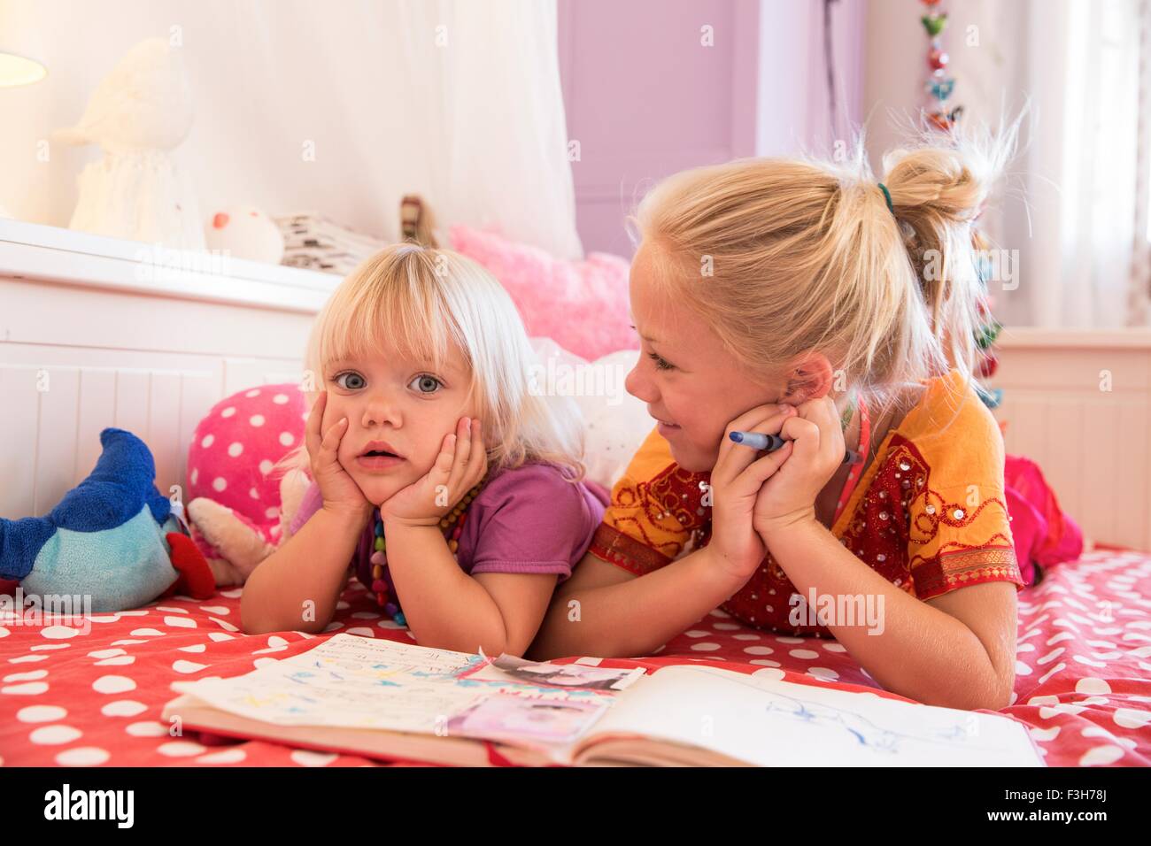 Girl and toddler sister on bed playing with colouring book Stock Photo