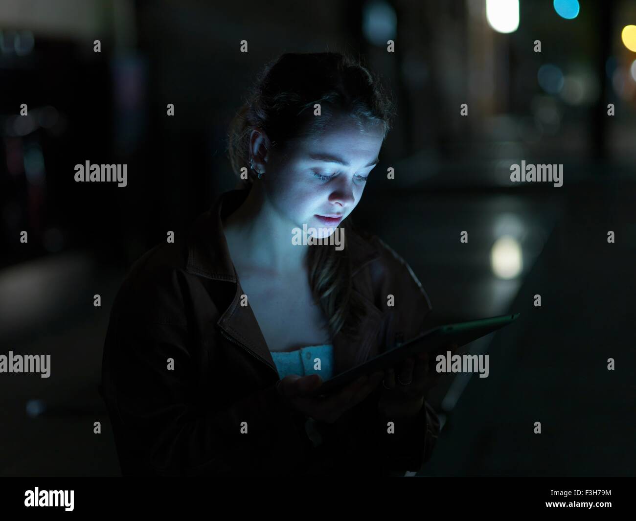 Young woman using digital tablet, outdoors, at night, face illuminated Stock Photo