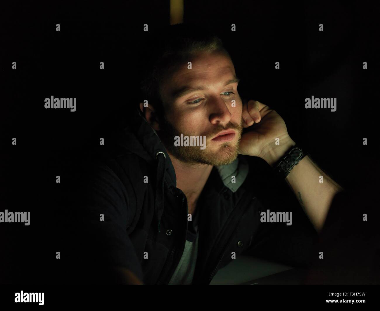 Young man using laptop at night, face illuminated Stock Photo