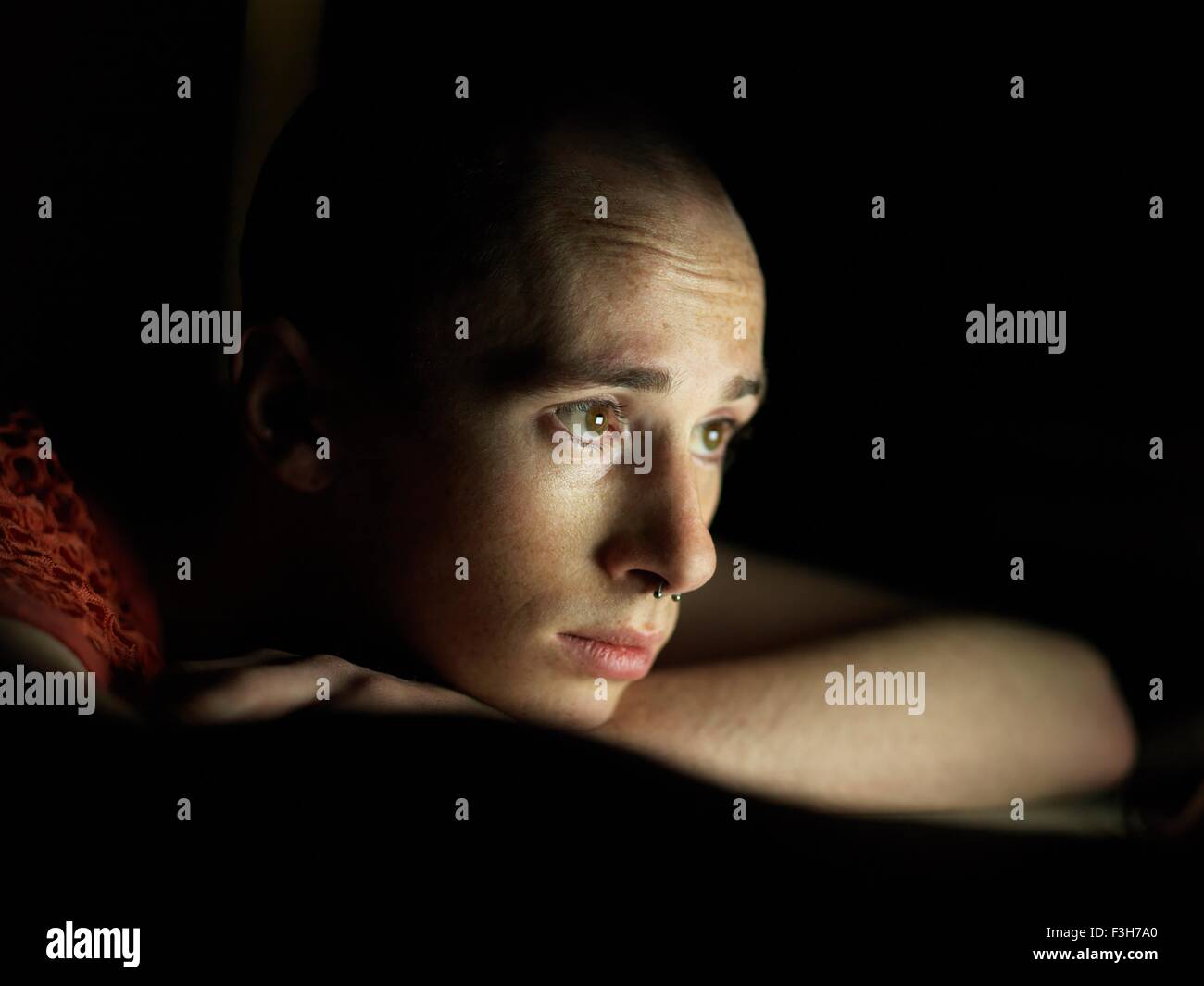 Young man sitting in dark, face illuminated Stock Photo