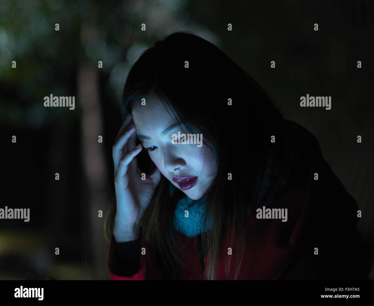 Young woman outdoors at night, using mobile phone, face illuminated Stock Photo