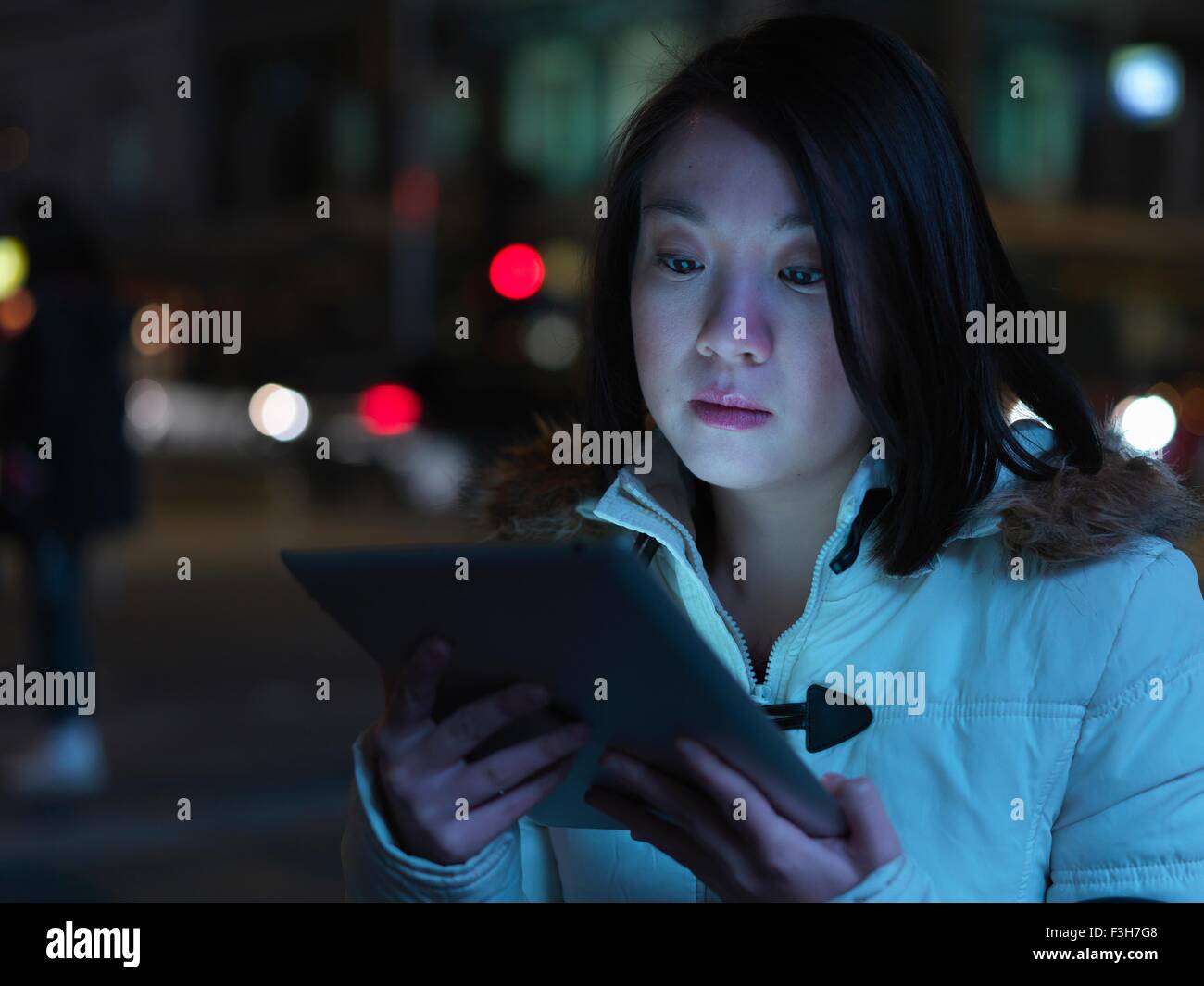 Young woman in street, at night, using digital tablet Stock Photo