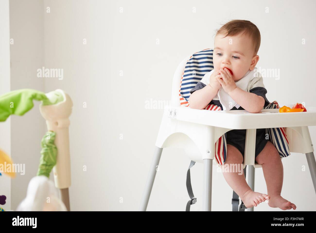 Baby boy feeding himself in baby chair Stock Photo