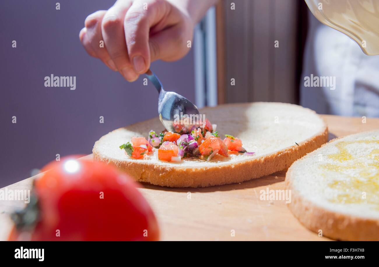 Hands of woman spreading ingredients on bread at kitchen counter Stock