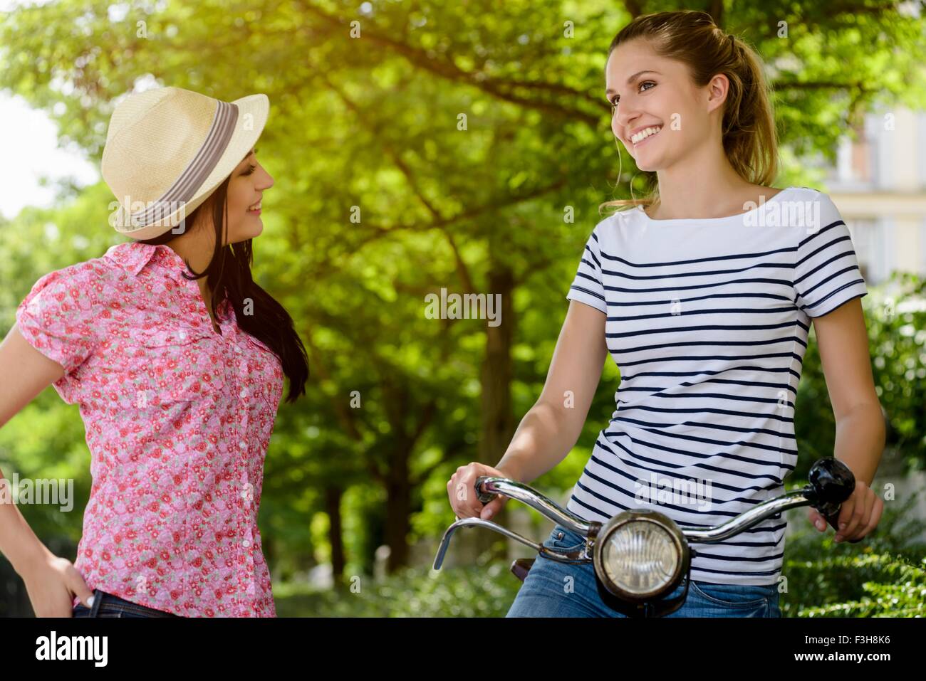 Young woman on bicycle talking to young woman wearing panama hat Stock Photo
