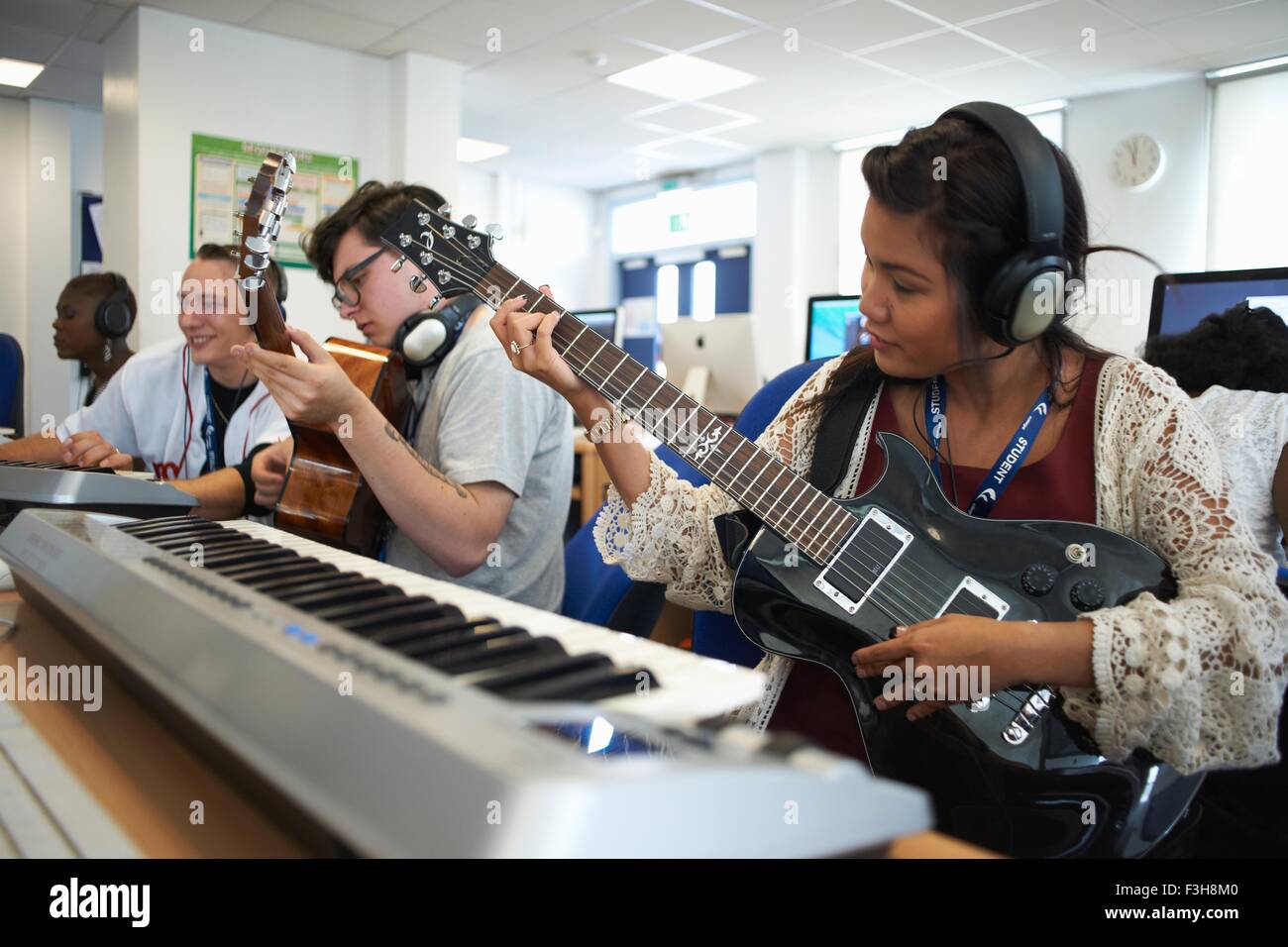 Small group of college students sitting in front of keyboards wearing headphones playing guitars Stock Photo