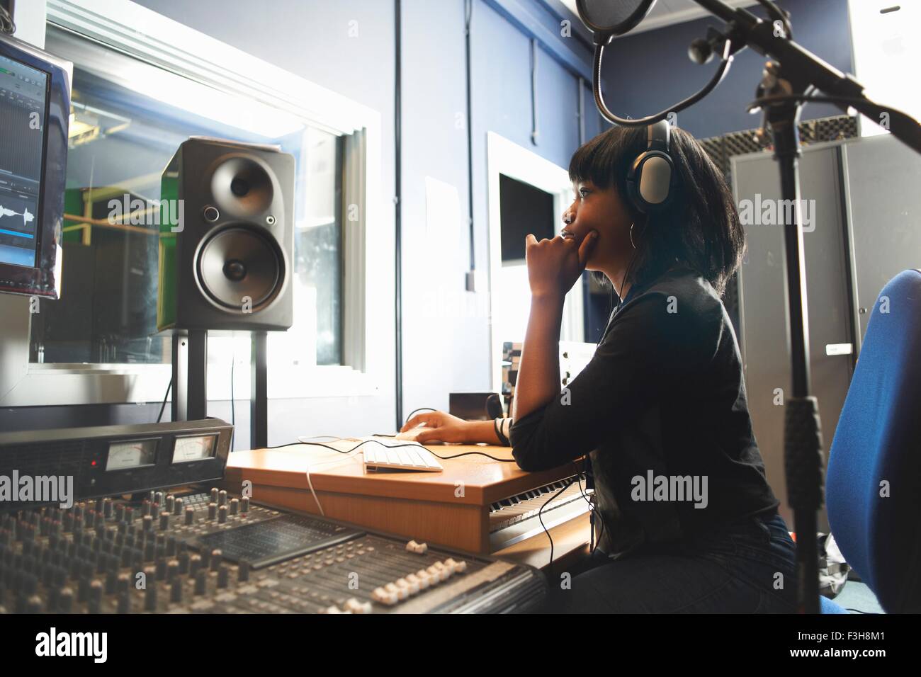 Side view of young woman wearing headphones, sitting at mixing desk in recording studio looking at monitor Stock Photo