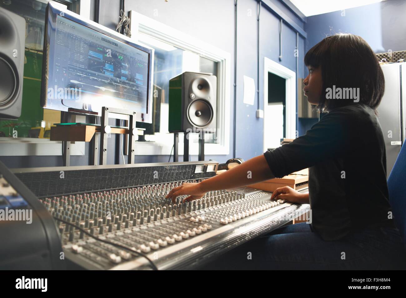 Side view of young woman sitting at mixing desk in recording studio looking at monitor, adjusting controls Stock Photo