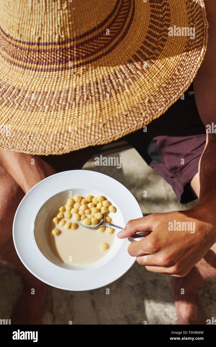 Cropped view of young man wearing sunhat eating breakfast cereal Stock Photo