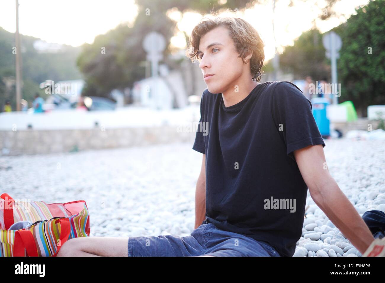 Young man sitting looking out from beach, Javea, Spain Stock Photo