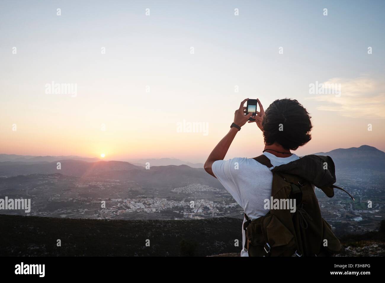 Rear view of young man photographing landscape and sunset on smartphone, Javea, Spain Stock Photo