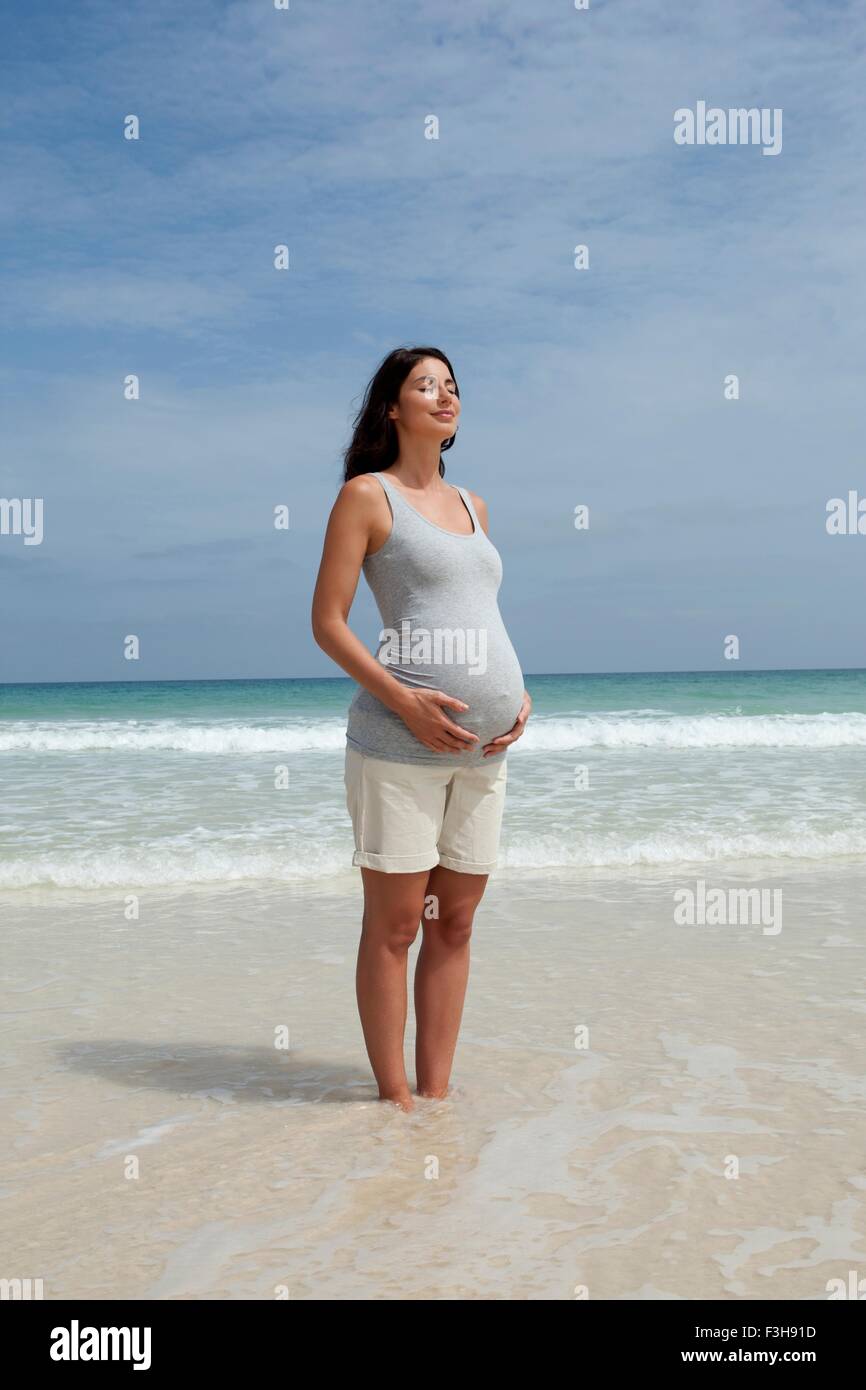 Pregnant mid adult woman standing with eyes closed in sea Stock Photo