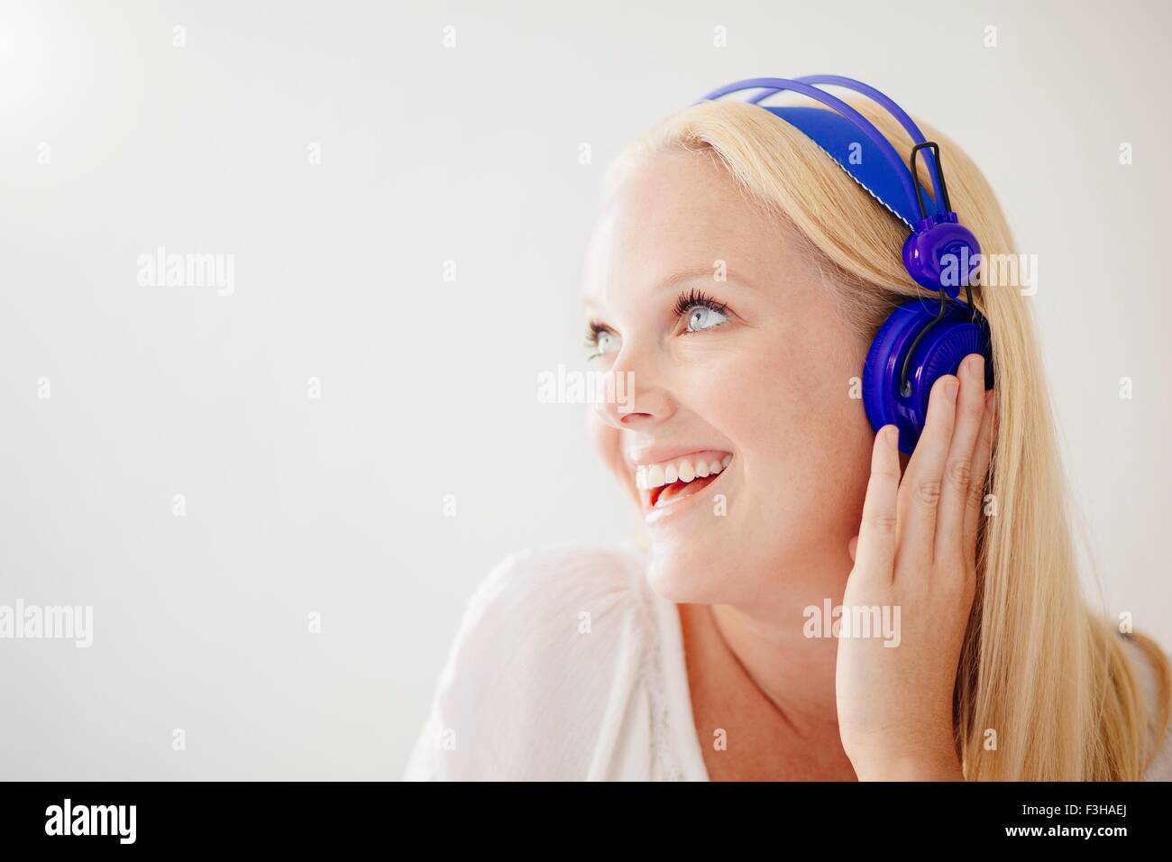 Young woman with long blonde hair wearing headphones looking away smiling Stock Photo