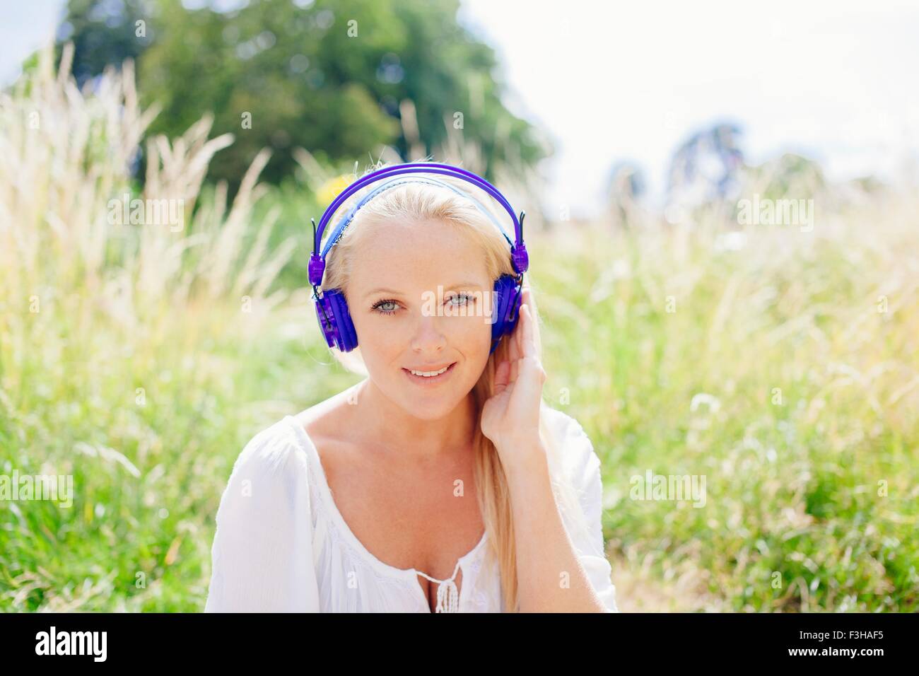 Portrait of young blonde woman wearing headphones looking at camera ...
