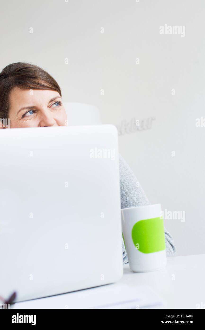 Mature woman sitting behind laptop, face obscured, looking away Stock Photo