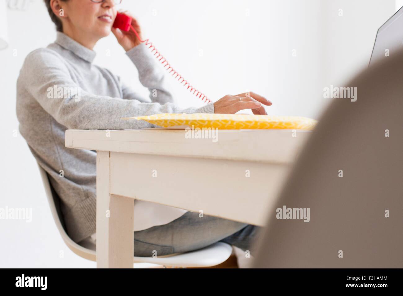 Cropped view of mature woman sitting at table using landline telephone, differential focus Stock Photo