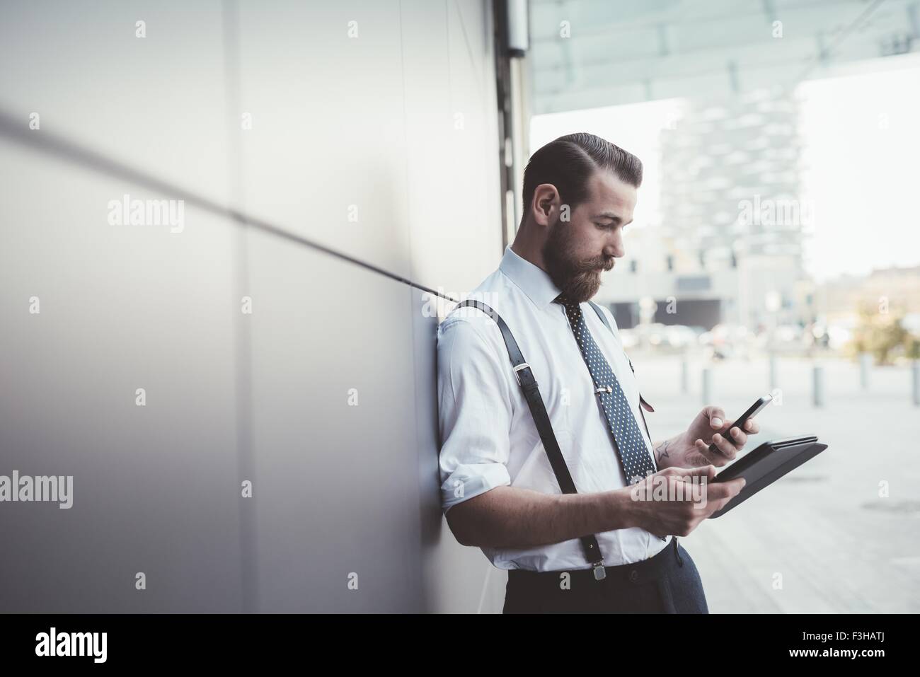 Stylish businessman using smartphone and digital tablet outside office Stock Photo