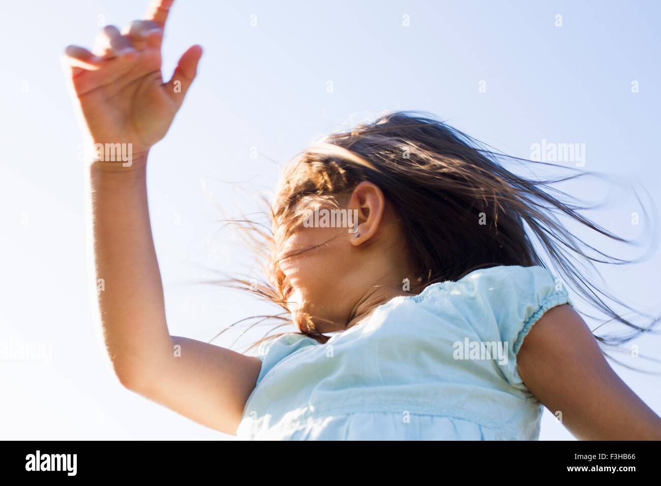 Low angle view of girl spinning around against blue sky Stock Photo