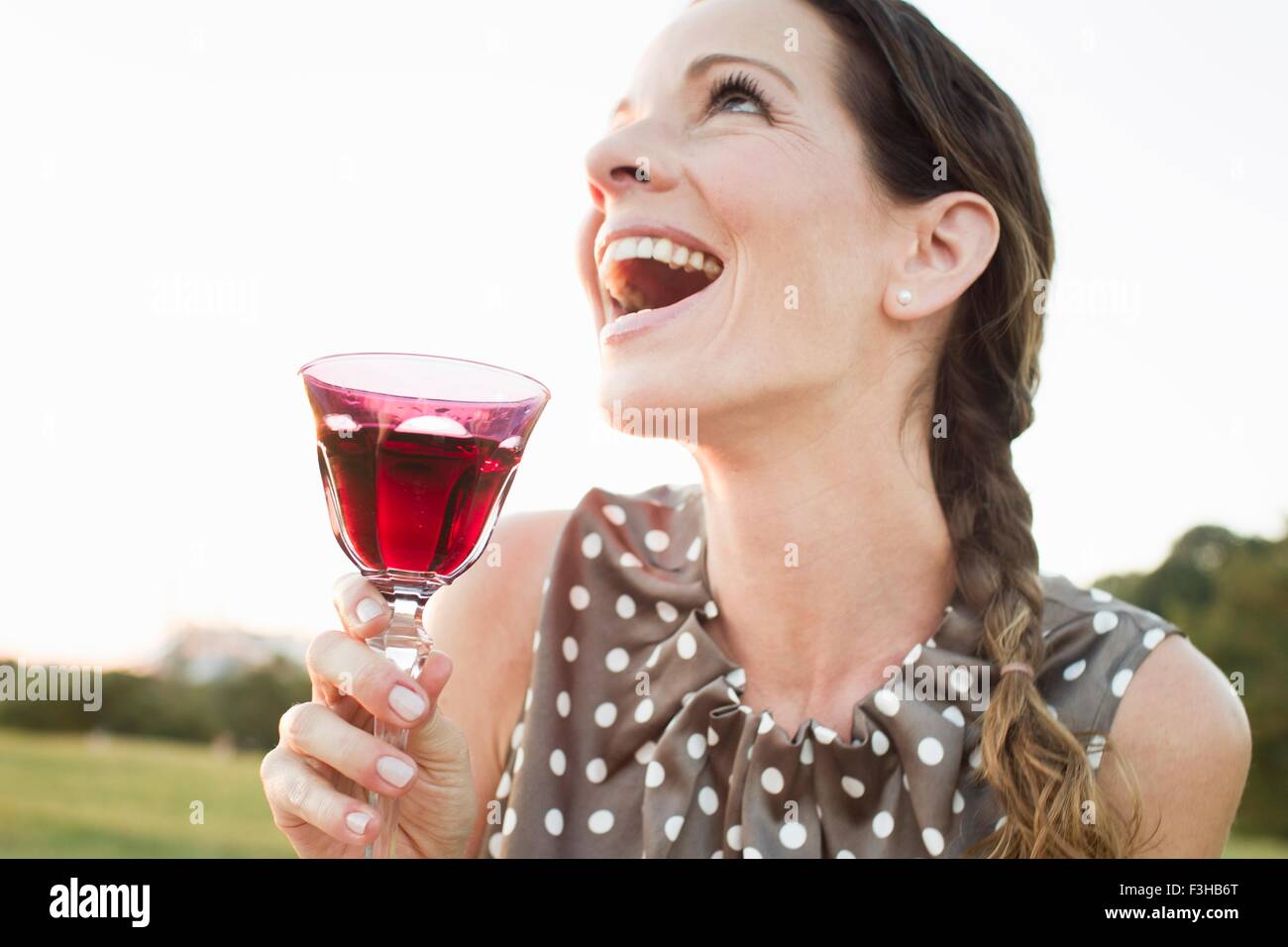 Mature woman laughing whilst drinking glass of red wine in park Stock Photo