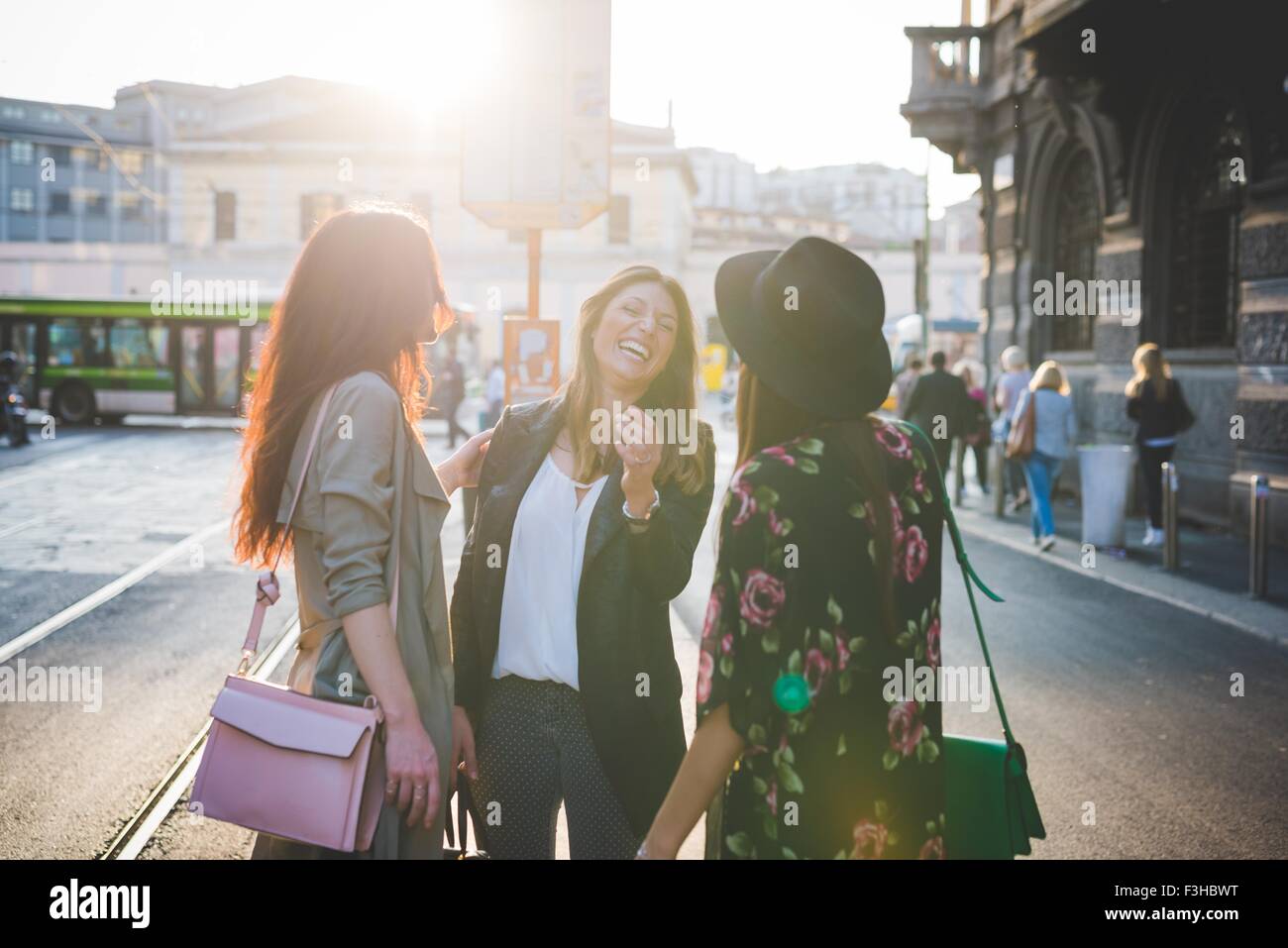 Three young women chatting and laughing on city street Stock Photo - Alamy
