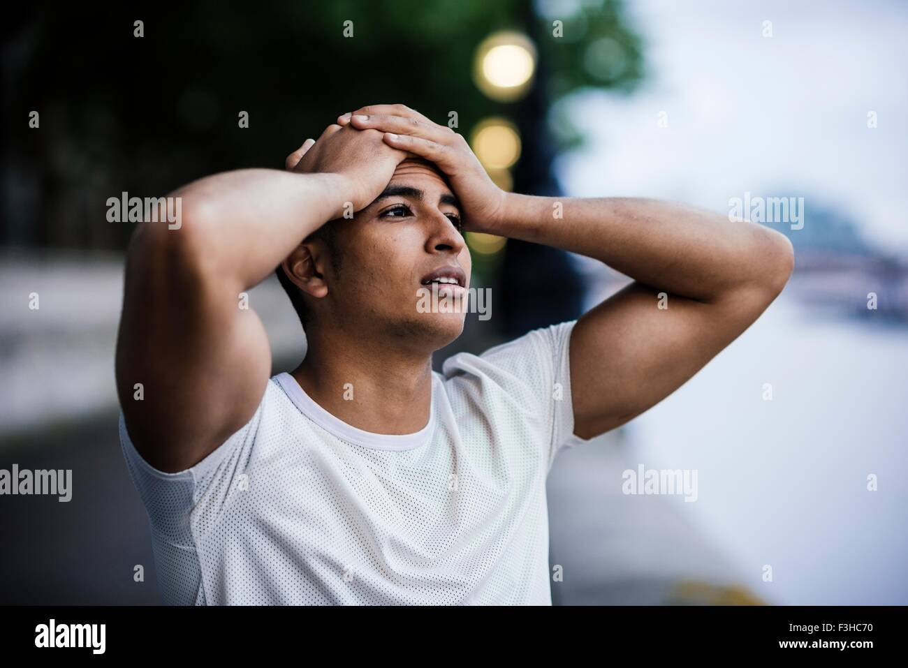 Male runner with hands on forehead taking a break on riverside Stock Photo