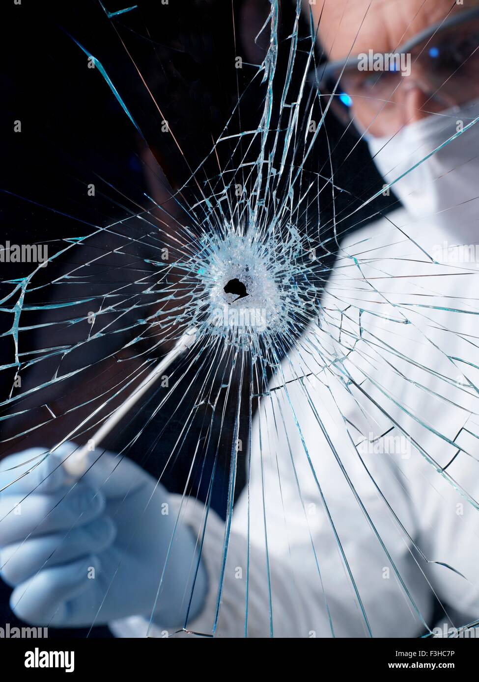 Forensics officer using swab to collect evidence from broken window Stock Photo