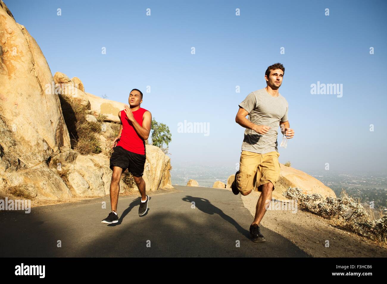 Two male friends running along mountain path Stock Photo