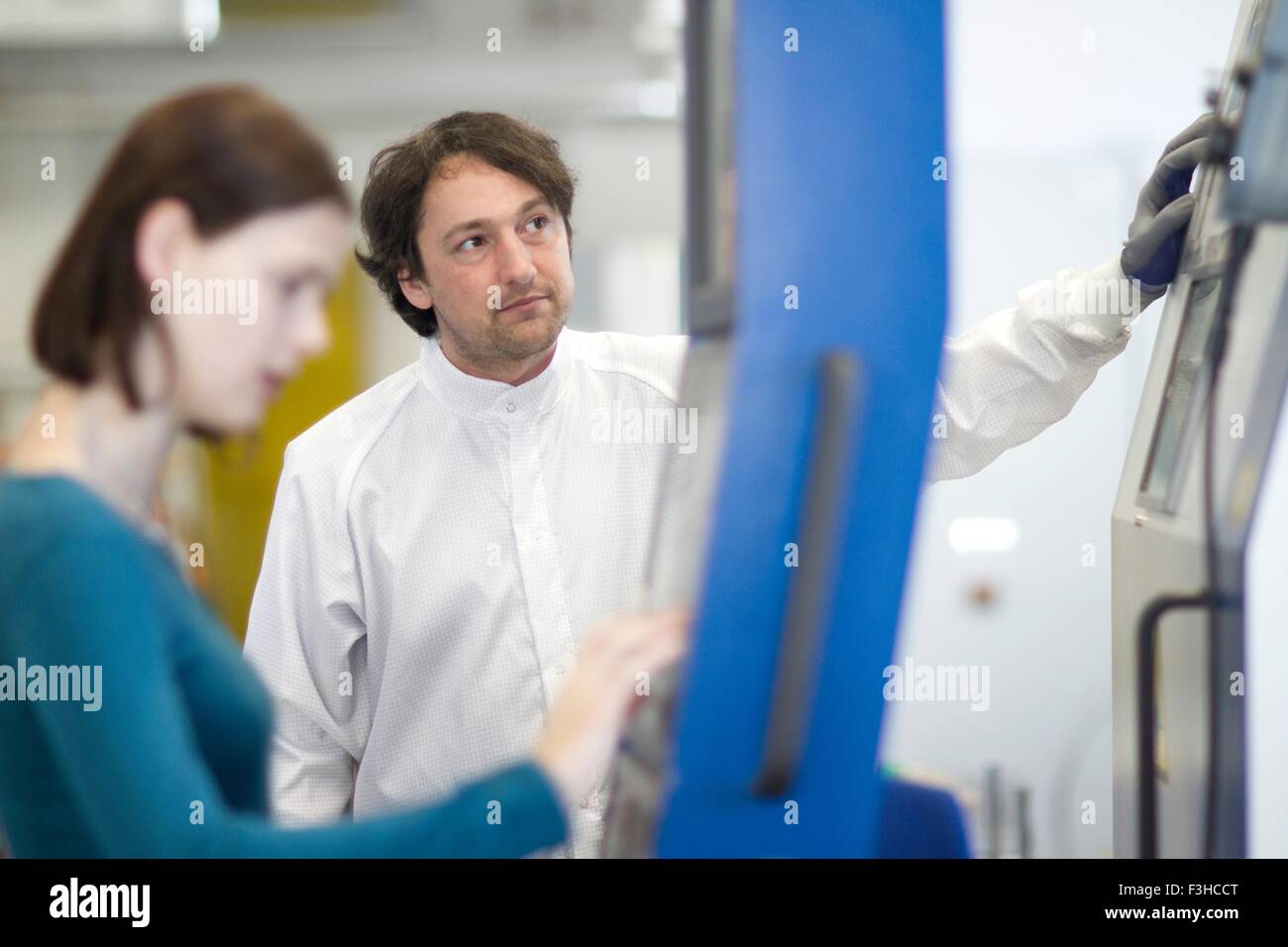 Mid adult man wearing labcoat and protective gloves operating machine, looking away Stock Photo