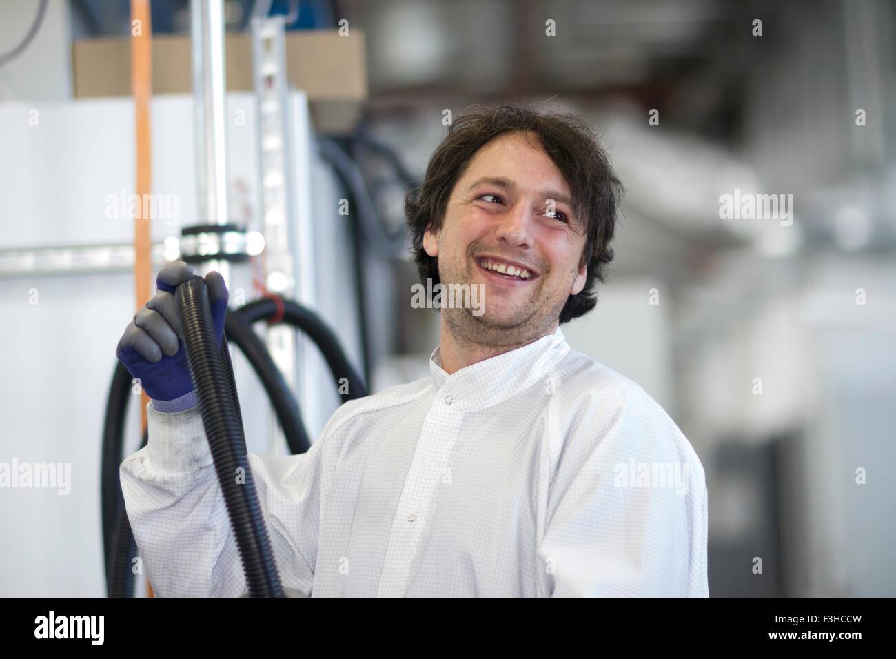 Mid adult man wearing labcoat holding industrial piping, looking away smiling Stock Photo