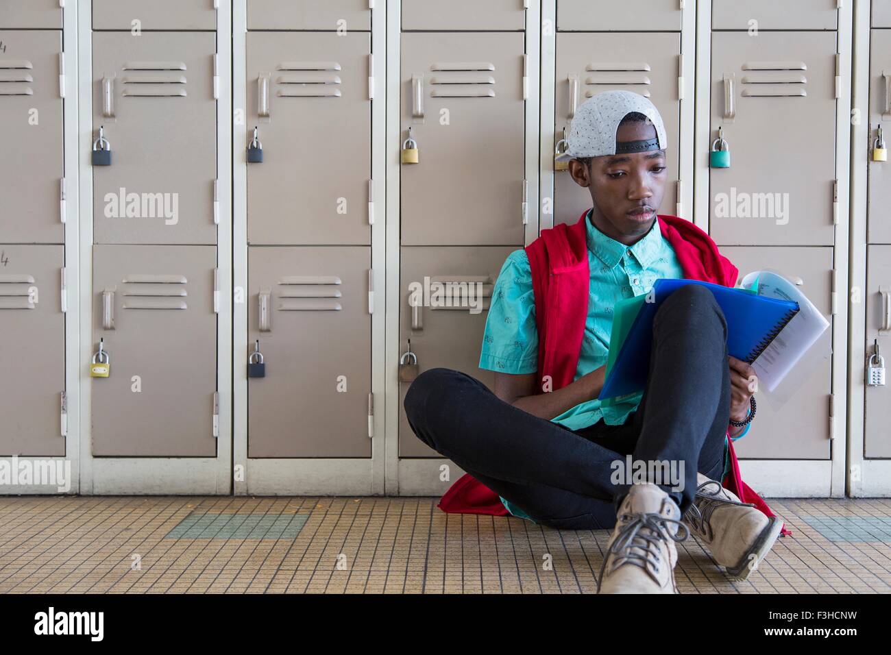 Student leaning against lockers, reading textbook Stock Photo