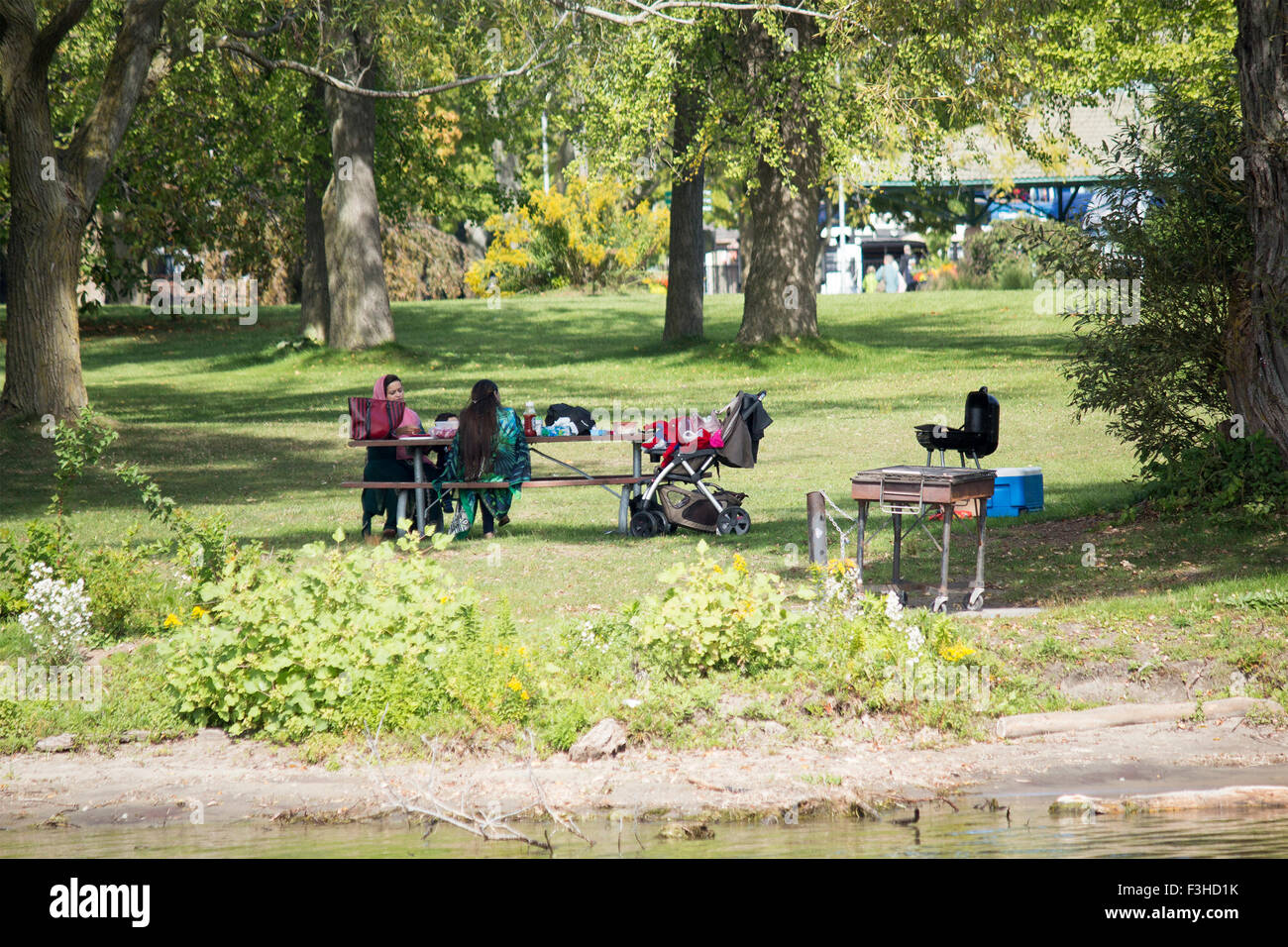 Two Muslim women sitting at a picnic table on Centre Island with child stroller relaxing on a sunny day. Stock Photo