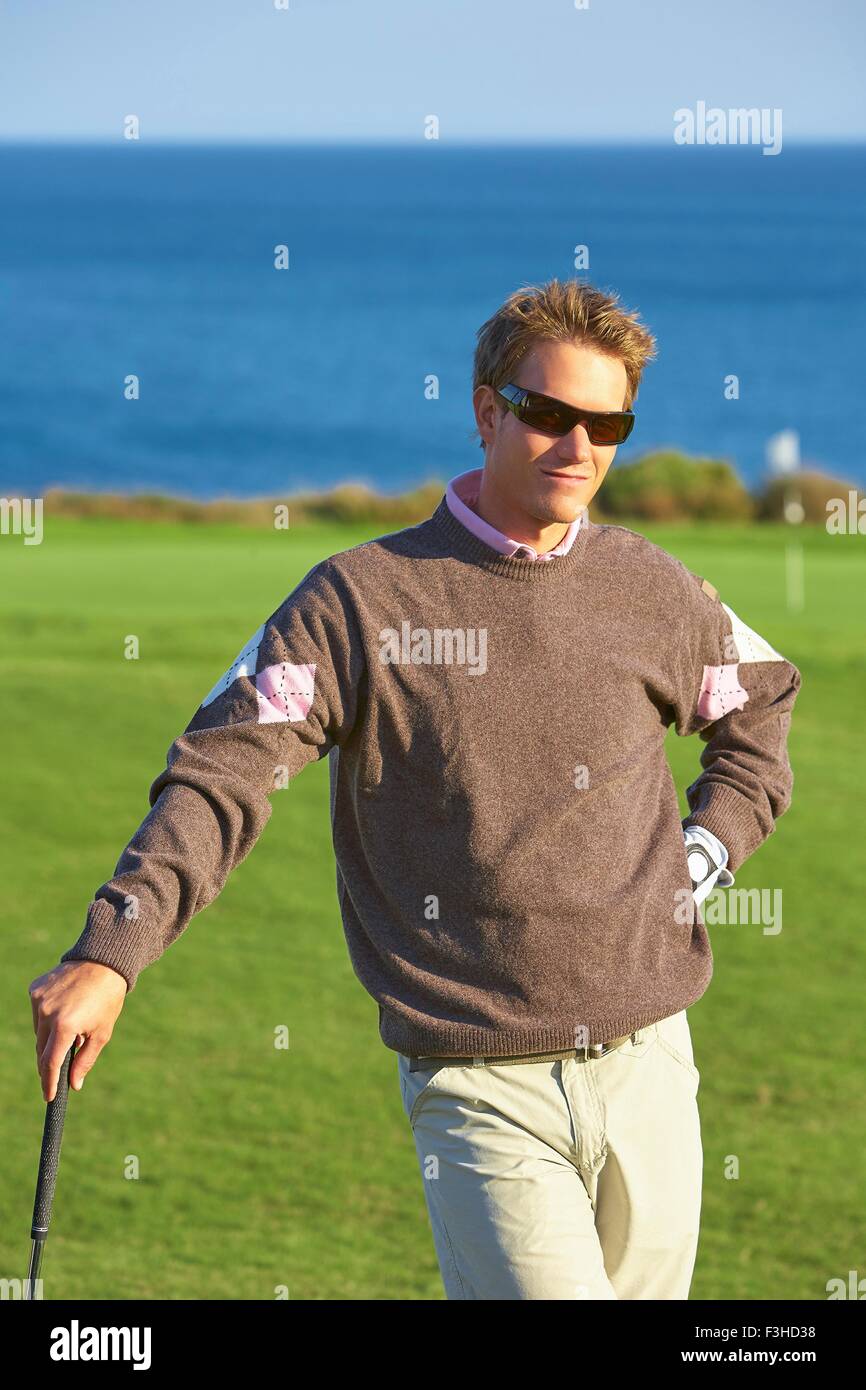 Golfer wearing sunglasses leaning against golf club, hand on hip