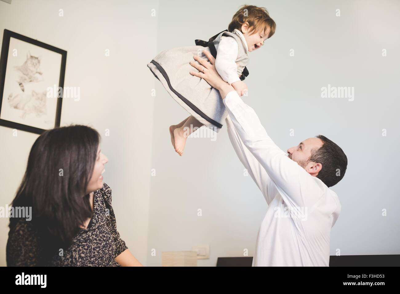 Mid adult man lifting up toddler daughter in living room Stock Photo
