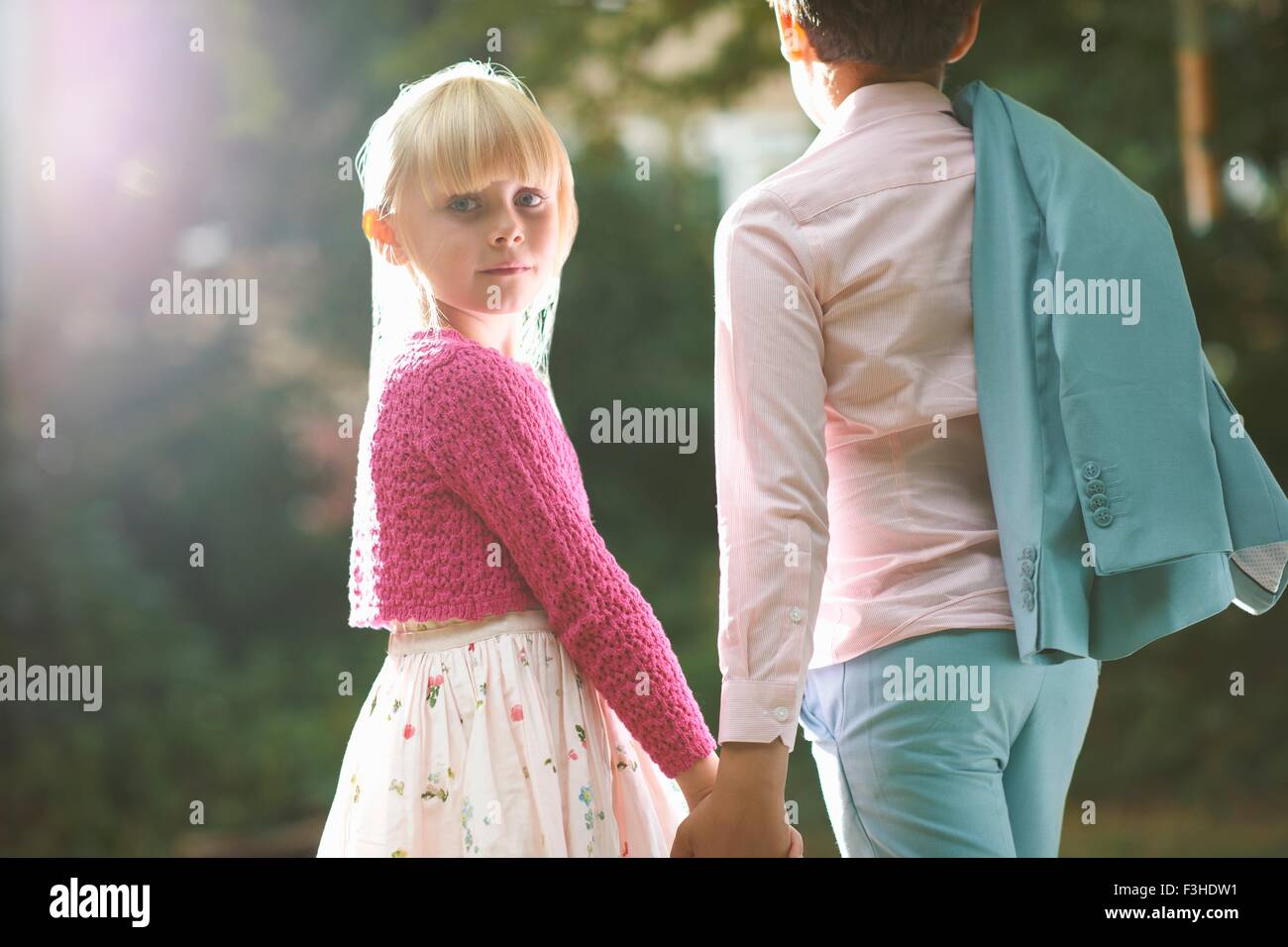 Girl looking over her shoulder whilst holding boys hand in garden Stock