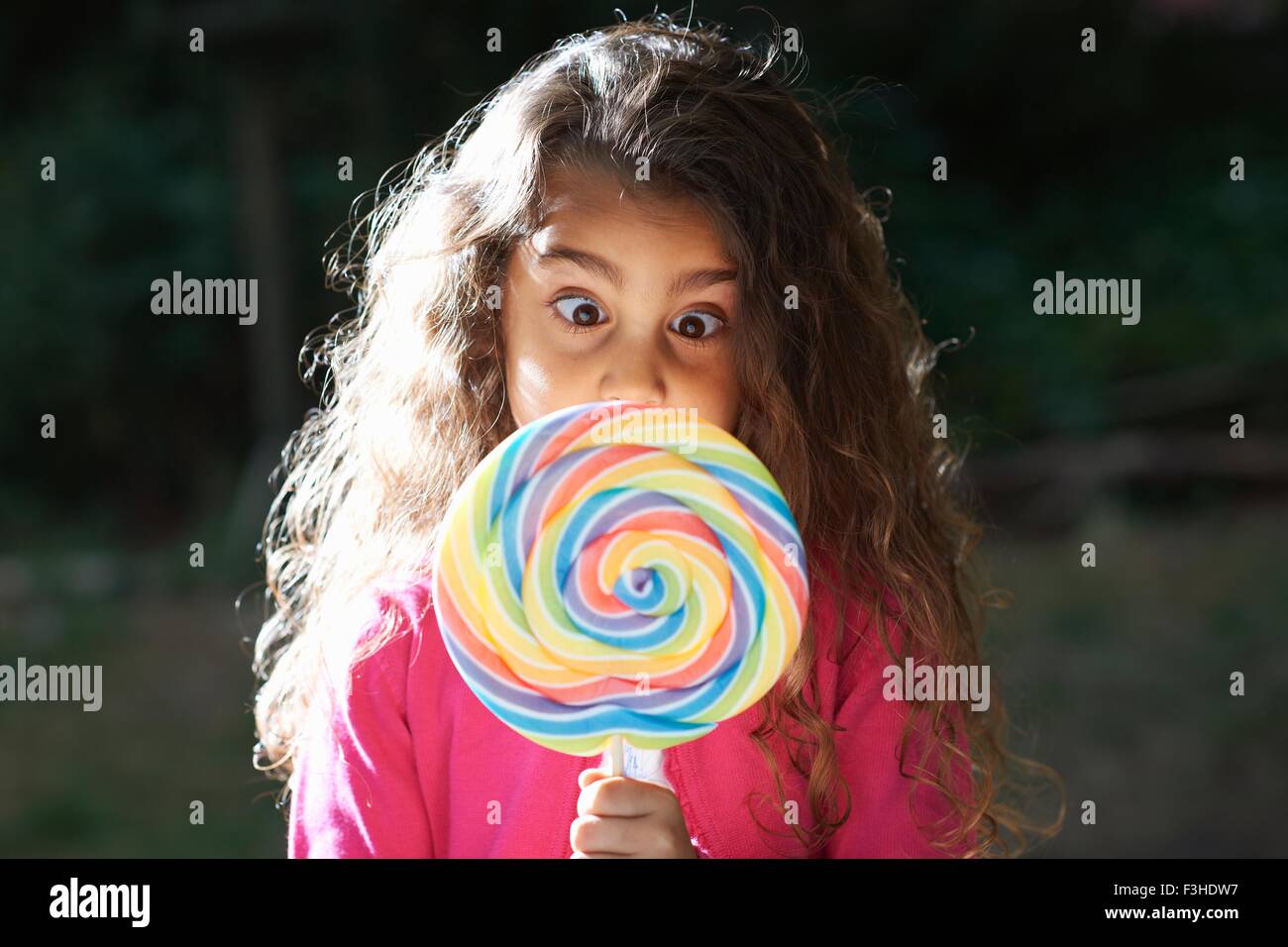 Portrait of girl crossing eyes with lollipop in front of her face in garden Stock Photo