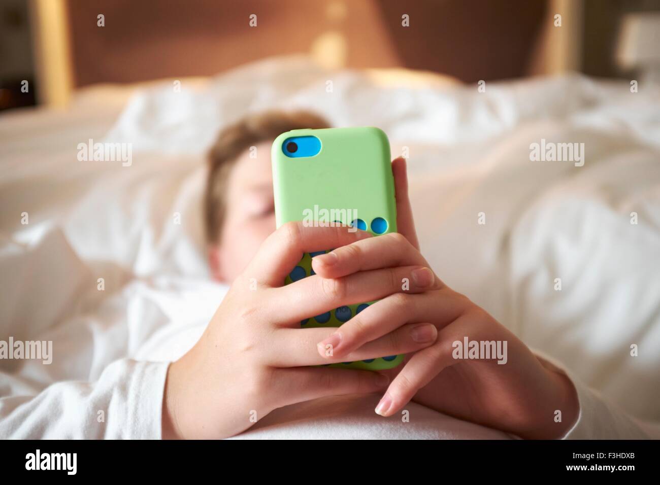 Close up of teenage boys hands holding smartphone on bed Stock Photo