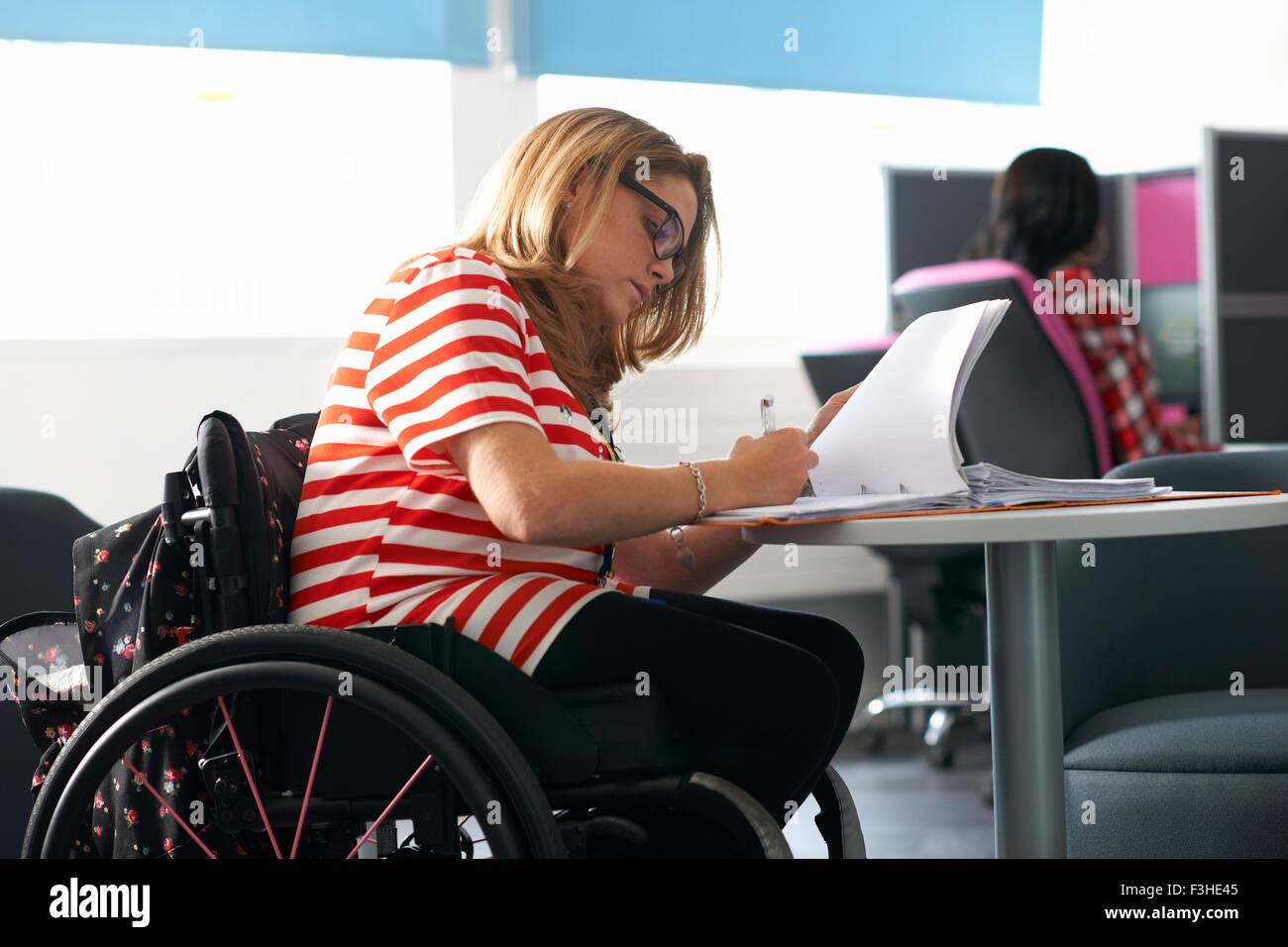 Teenage girl in wheelchair writing up notes in class Stock Photo