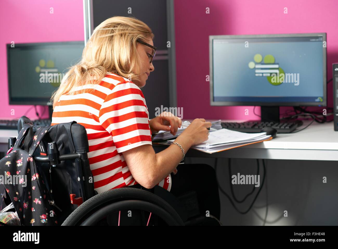 Teenage girl in wheelchair writing up file notes in class Stock Photo