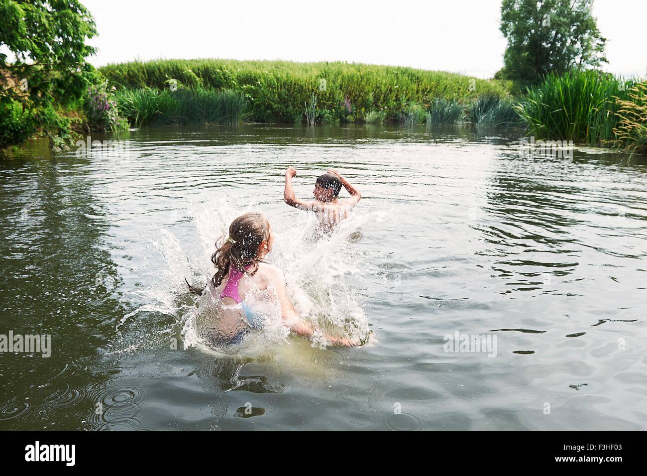 Teenage boy and sister splashing in rural lake Stock Photo