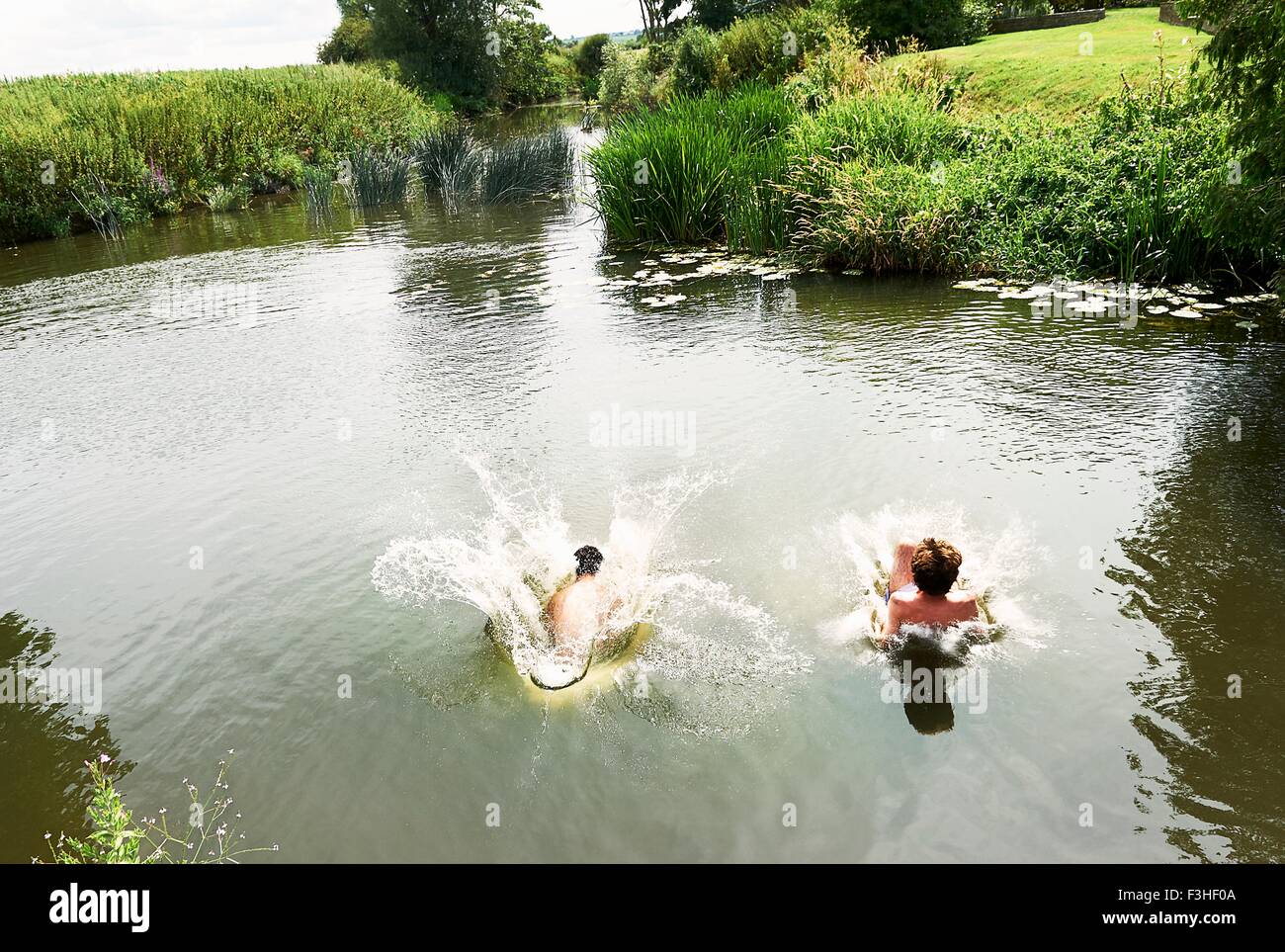 Young man and teenage boy splashing into rural lake Stock Photo