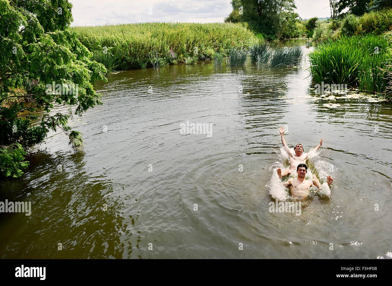 Young man and teenage boy splashing in rural lake Stock Photo