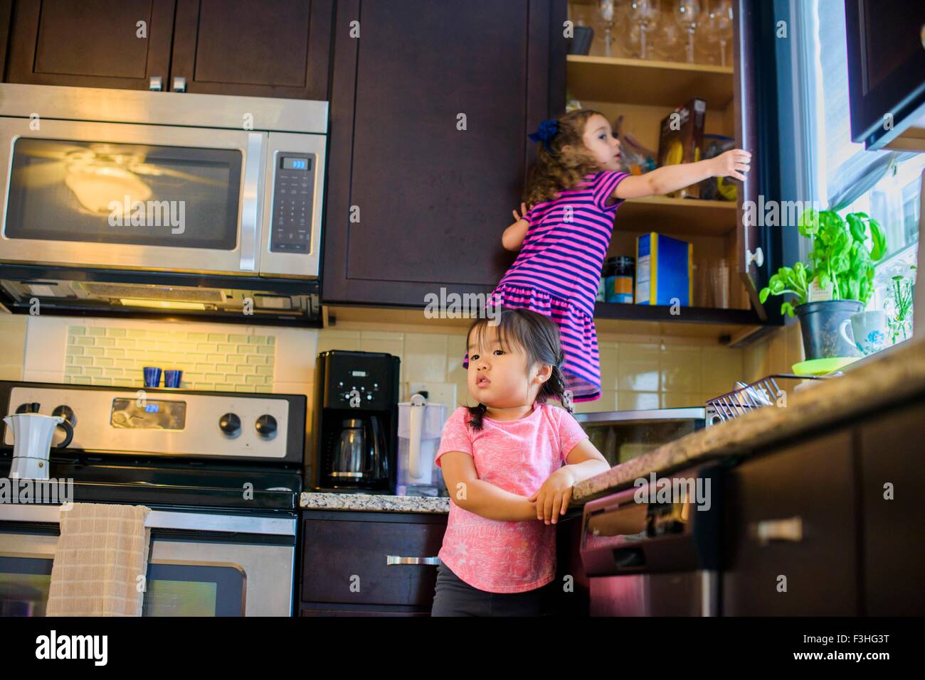 Young girl standing on kitchen work surface, looking for treats in cupboard Stock Photo