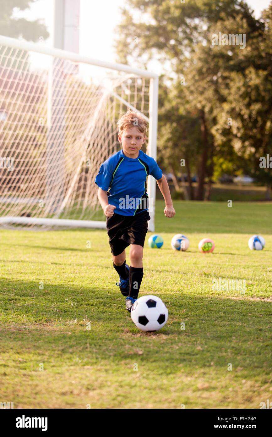 Boy running with football on practice pitch Stock Photo Alamy