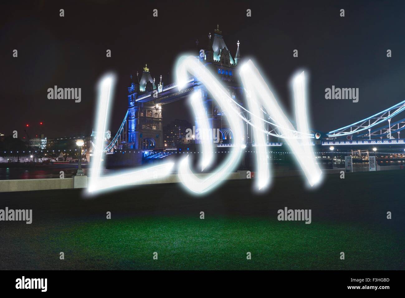 Glowing abbreviated London symbol in front of Tower Bridge at night Stock Photo