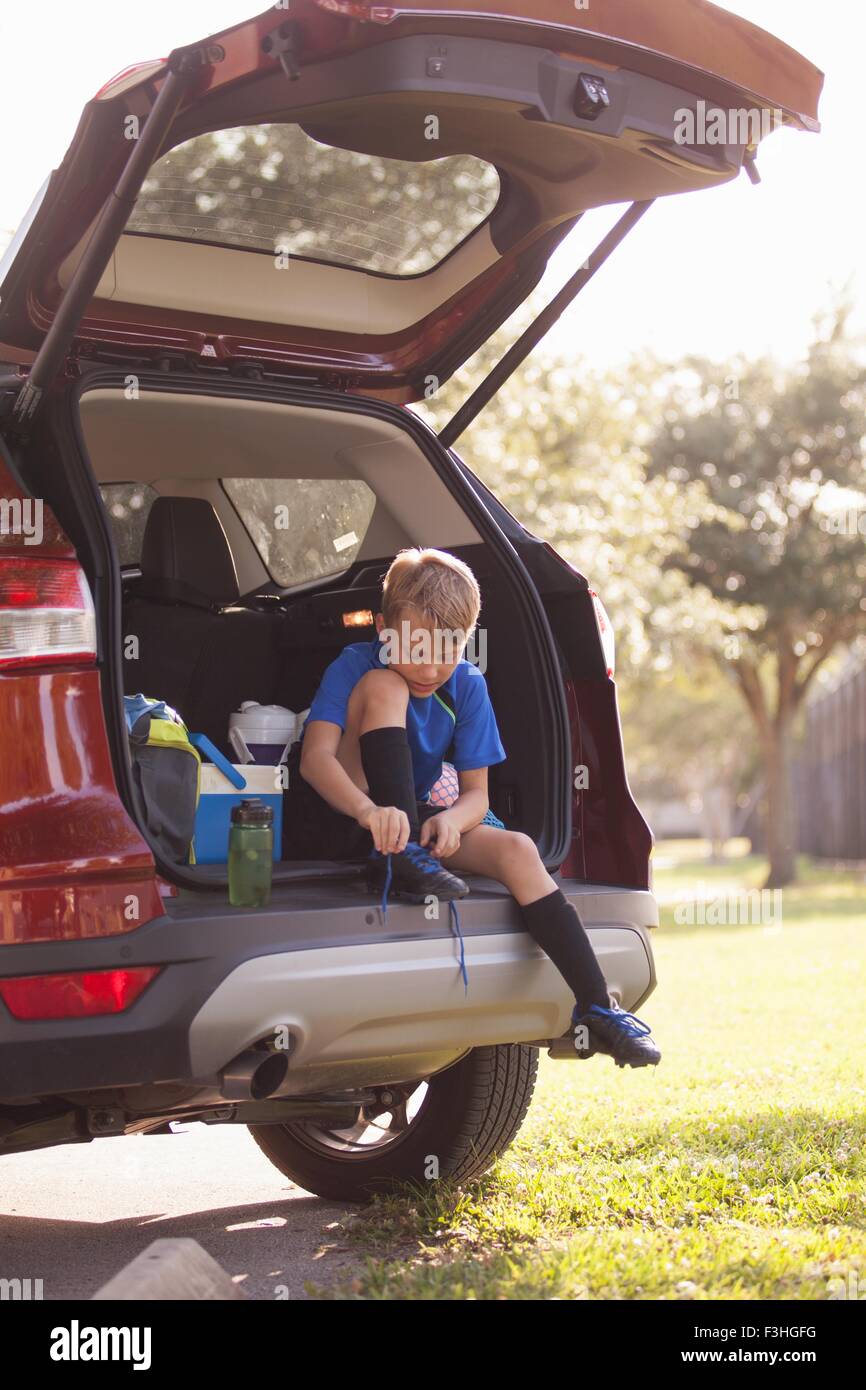 Boy football player sitting in car boot tying football boot laces Stock