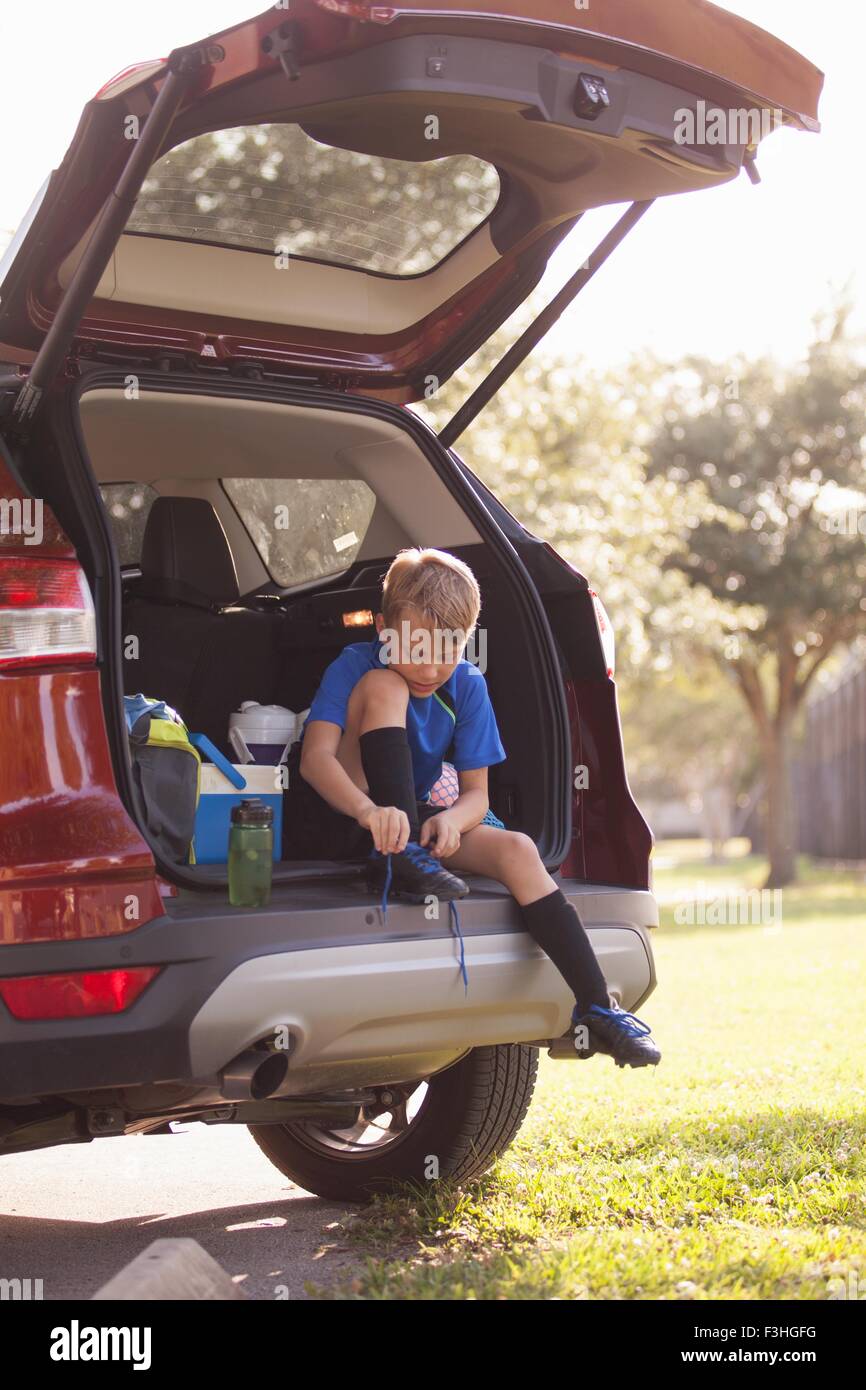 Boy football player sitting in car boot tying football boot laces Stock Photo