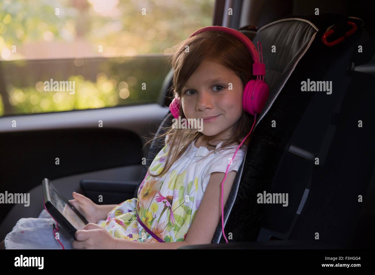 Portrait of girl wearing pink headphones and using digital tablet in car Stock Photo