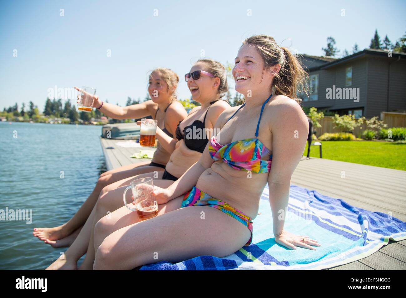 Three young women wearing bikinis drinking beer on waterfront pier, Lake Oswego, Oregon, USA Stock Photo