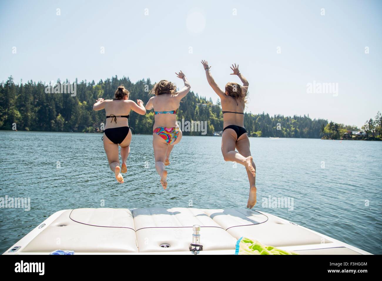 Rear view of three young women jumping from pier, Lake Oswego, Oregon, USA Stock Photo