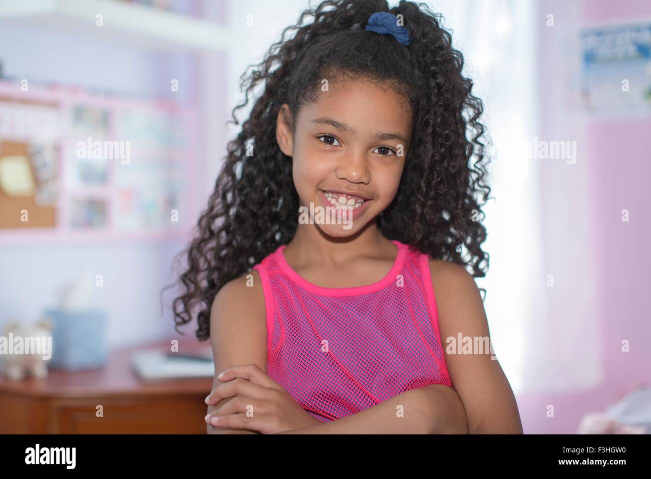Portrait of girl with black curly hair, arms folded, looking at camera smiling Stock Photo